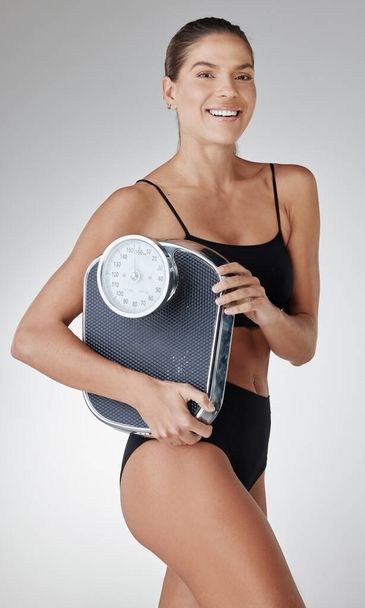 Scale down on bad food, beef up on the good. Studio shot of an attractive and fit young woman holding a scale against a grey background - Foto, Bild
