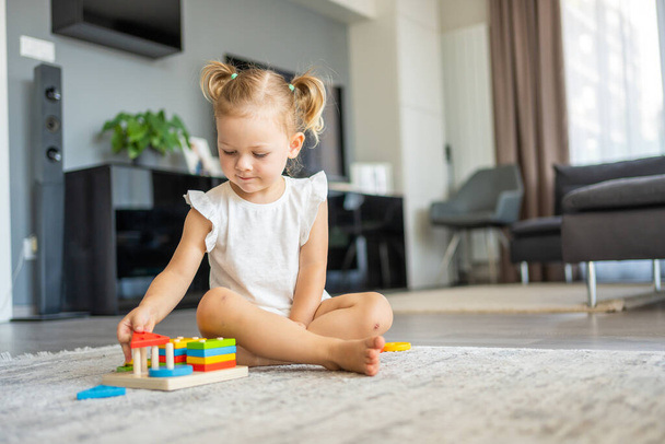 Schattig blank klein meisje dat thuis op de vloer speelt met eco houten speelgoed. Het kind speelt educatieve spelletjes. Hoge kwaliteit foto - Foto, afbeelding