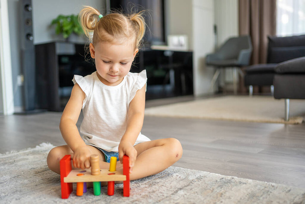 Schattig blank klein meisje dat thuis op de vloer speelt met eco houten speelgoed. Het kind speelt educatieve spelletjes. Hoge kwaliteit foto - Foto, afbeelding