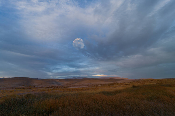 Moon rising against a cloudy sky shown in the Mojave Desert in California.  - Foto, Bild
