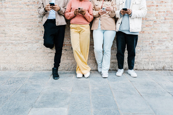 Group of young teen people using smart mobile phones outdoor. Unrecognizable multiracial people holding smart phone while lying on brick wall in city street. Copy space for text - Φωτογραφία, εικόνα