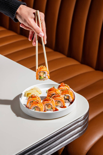 California roll with salmon, Philadelphia cheese, eel and avocado. Top the sushi with unagi sauce. lies red caviar and finely chopped green onions. The food is in a white, ceramic plate with high sides, next to it is a square of wasabi and pickled gi - Фото, изображение