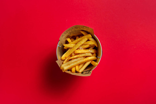 Fried fries with salt in a small bucket on a red background - Фото, зображення
