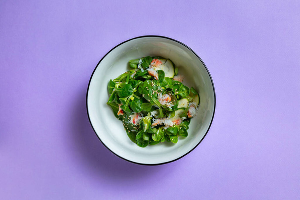 Salad with crab meat, sesame seeds, basil, zucchini and mung bean salad in a plate on a lilac background - 写真・画像