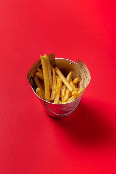 Fried fries with salt in a small bucket on a red background - Foto, imagen