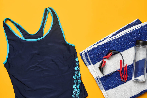 Flat lay summer pool accessories such as blue swimwear, red swimming goggles, striped towel and transparent bottle on a yellow background. Colorful beach wear. Copy space, top view, close-up. - 写真・画像