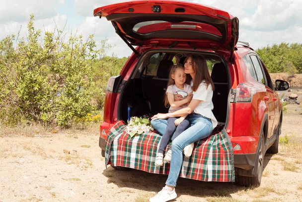 Beautiful Ukrainian girl. Mother and daughter photo session. A woman in a car. Photo session in the trunk of the car. Summer cozy photo shoot. - Фото, изображение