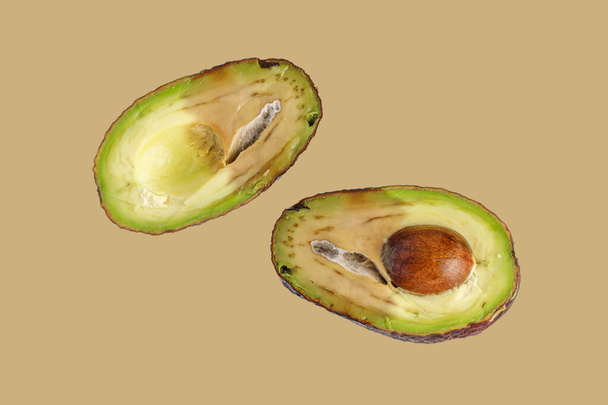 Rotten unhealthy sliced Haas avocado isolated on beige neutral background. Food waste. - Photo, Image