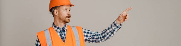 White man worker wearing helmet pointing finger aside isolated over grey background - Foto, Imagen