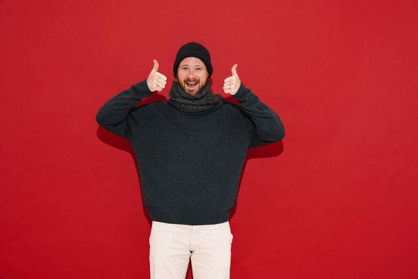 White man wearing warm clothes smiling and showing thumbs up isolated over red background - Фото, зображення