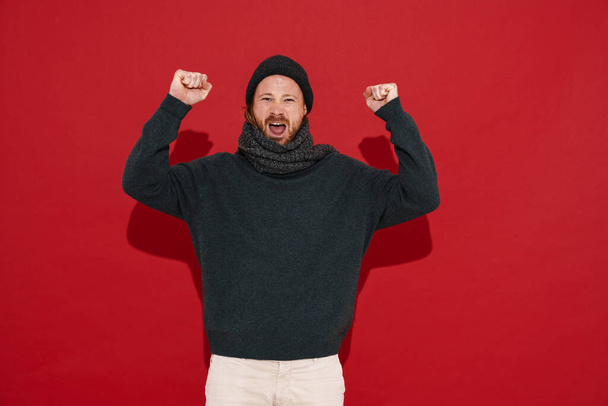 White man wearing warm clothes screaming and showing winner gesture isolated over red background - Фото, зображення