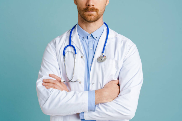 White male doctor wearing lab coat posing with stethoscope isolated over blue background - Foto, Imagem