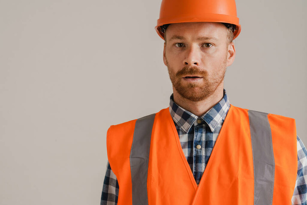 White man worker wearing helmet and vest looking at camera isolated over grey background - Photo, Image