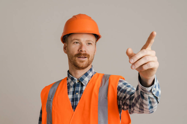 White man worker wearing helmet pointing finger aside isolated over grey background - Foto, afbeelding