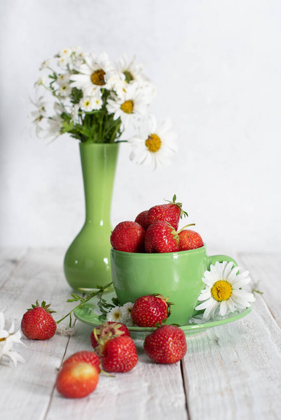ripe strawberries from the garden in a green mug with white chamomile, fruity summer still life, close-up. High quality photo - 写真・画像
