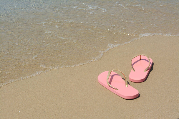 Stylish pink flip flops on wet sand near sea, space for text - Foto, afbeelding
