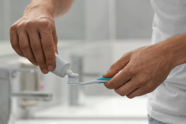 Man applying toothpaste on brush in bathroom, closeup - Fotoğraf, Görsel