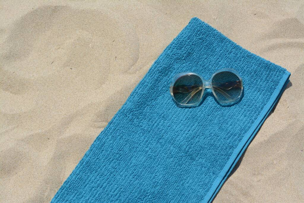 Soft blue beach towel with sunglasses on sand, top view. Space for text - Photo, image