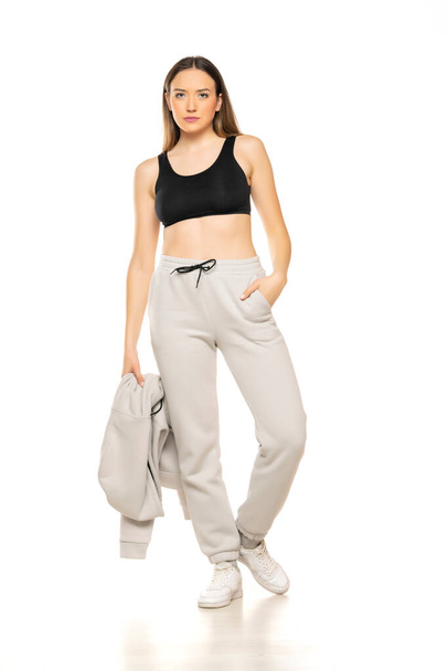 a young woman in a gray tracksuit and black top poses against a white background in the studio. - Foto, Imagen
