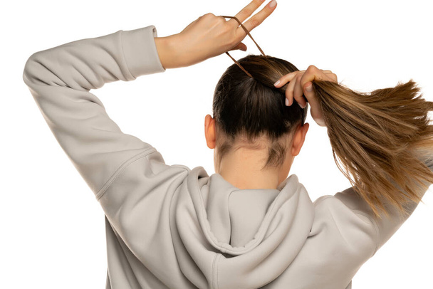 a young woman in a gray tracksuit ties a pony tail to a white background in the studio. - Foto, immagini