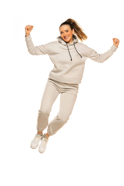 a young happy woman in a gray tracksuit jumping against a white background in the studio. - Foto, Imagen