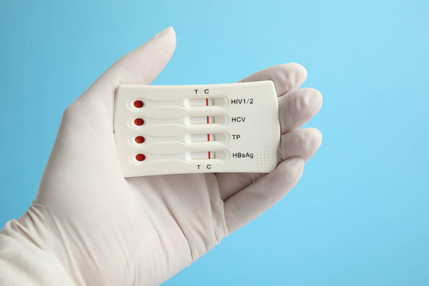 Doctor holding disposable express test for hepatitis on light blue background, closeup - 写真・画像