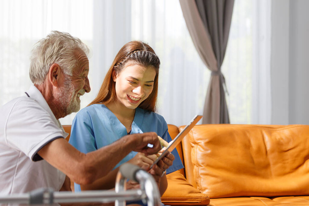 professional female doctor using digital tablet Senior male patient medical test results explain prescription using tablet app sitting on the sofa at home Elderly health care technology concept - 写真・画像