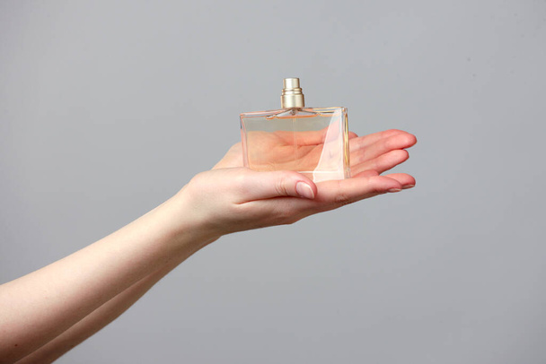 Perfume bottle in beautiful woman hands on grey background - 写真・画像