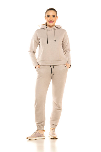 Front view of a young smiling woman in a gray tracksuit posing to a white background in the studio. - Фото, изображение