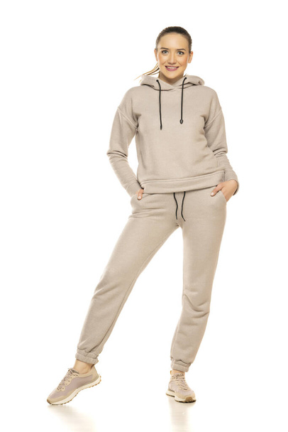 Front view of a young smiling woman in a gray tracksuit posing to a white background in the studio. - Foto, imagen