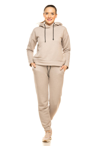 Front view of a young smiling woman in a gray tracksuit walking to a white background in the studio. - Foto, Imagem
