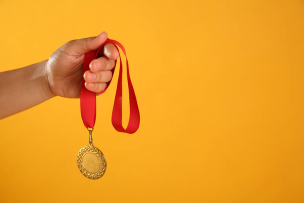 Woman holding gold medal on yellow background, closeup. Space for text - Foto, Imagen