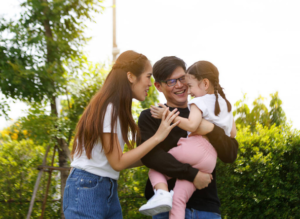 Asian family, bright and cute daughters are relaxing as parents walk their children on the clear blue lawn and green trees look after them behind them. Concept of happy family relationship, lifestyle - Photo, Image