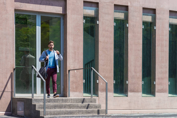 Businessman walking next to office buildings while holding a shoulder bag - Fotoğraf, Görsel