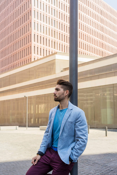 Bearded man, model of fashion, in urban background wearing casual clothes while leaning on a streetlight pole - Foto, immagini