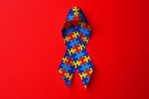 World Autism Awareness Day. Colorful puzzle ribbon on red background, top view - Foto, immagini