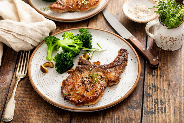 Grilled or pan fried pork chops on the bone with garlic and rosemary served with broccole for dinner - Фото, изображение