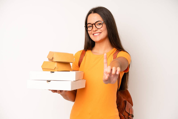 hispanic pretty woma looking surprised and shocked, with jaw dropped holding an object. delivery take away concept - Foto, Bild
