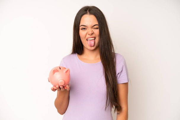 hispanic pretty woma looking shocked and surprised with mouth wide open, pointing to self. piggy bank savings concept - Foto, Imagem