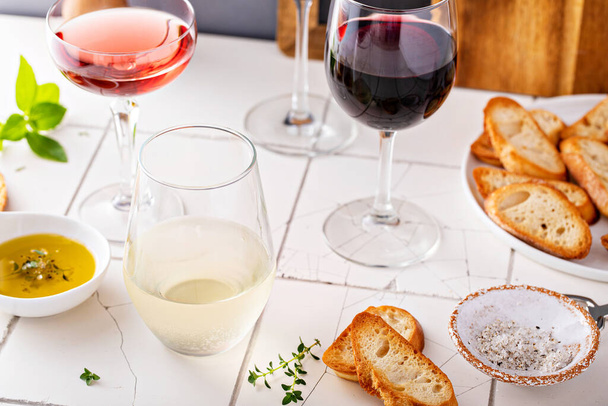 Variety of wine glasses with red, white and rose wine with toasted baguette and olive oil on the table - Zdjęcie, obraz
