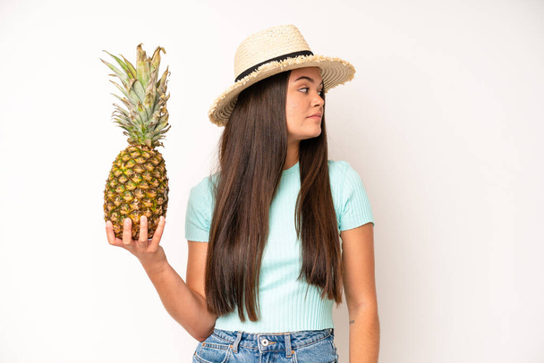 hispanic pretty woma with mouth and eyes wide open and hand on chin. pineapple and summer concept - Foto, Imagen