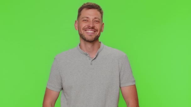 Bearded happy young man showing victory sign, hoping for success and win, doing peace gesture, smiling with kind optimistic expression. Adult guy isolated on green chroma key studio background indoors - Séquence, vidéo
