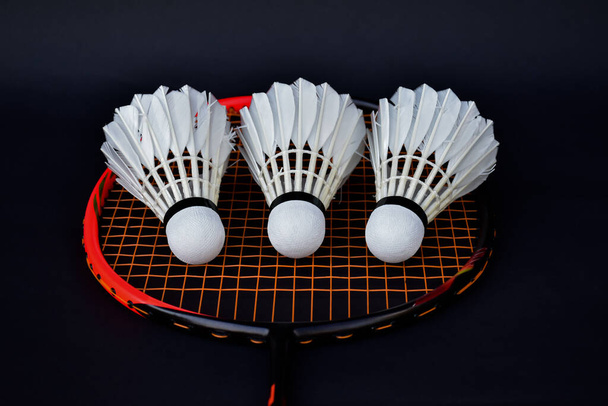 White cream badminton shuttlecocks, badminton rackets on dark floor of indoor badminton court, soft and selective focus on shuttlecock, concept for badminton sport lovers around the world - 写真・画像