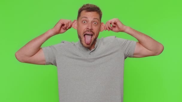 Bearded handsome funny man in t-shirt making playful silly facial expressions and grimacing, fooling around, showing tongue. Adult male guy isolated alone on chroma key studio background indoors - Filmagem, Vídeo