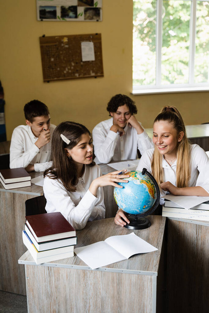 Children in geography lesson look at globe and discuss different countries. Education concept. Schoolchildren rotate globe and communicate with each other - Foto, Imagem