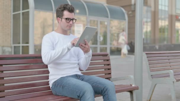 Casual Man using Tablet while Sitting Outdoor on Bench - Materiaali, video