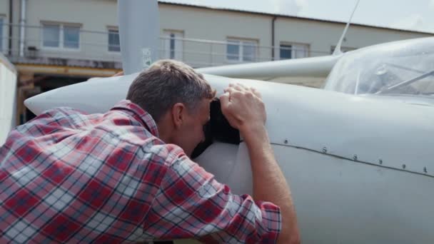 Private airplane engine inspection by aviation engineer close up. Focused white plane pilot checking aircraft parts preparing flying from airdrome. Aviator controlling work air transport outdoors. - Imágenes, Vídeo