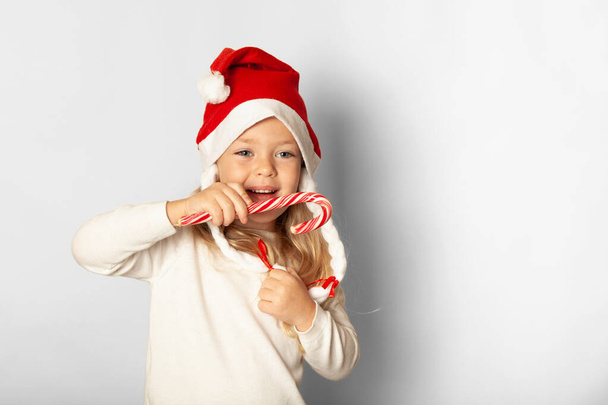 Portrait of little pretty girl in Santa hat with lollipop candy isolated on white background. Happy Christmas holidays, cute child in happiness. - Φωτογραφία, εικόνα