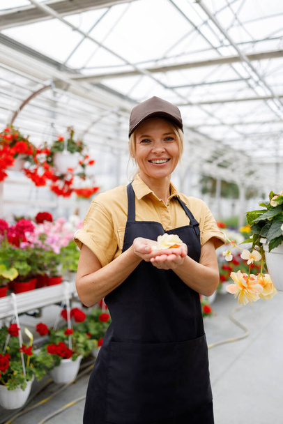 Portrait of female florist with flower petals in hands. Greenhouse worker at her lovely job - Фото, зображення