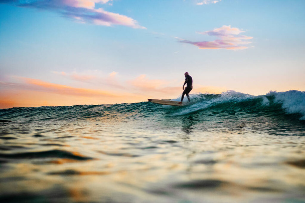 A male surfer on the sea waves at sunset - Fotoğraf, Görsel